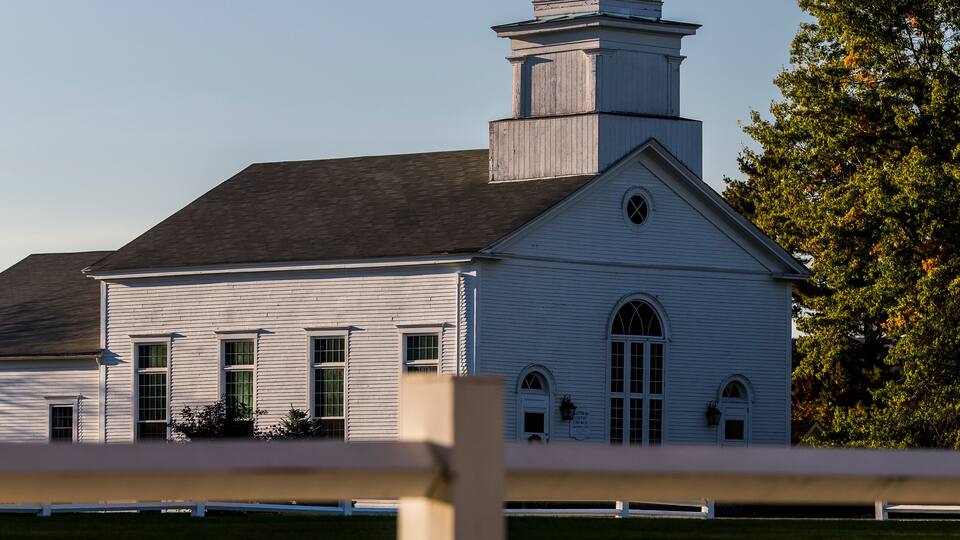 A white church with a steeple and a fence in the foreground.