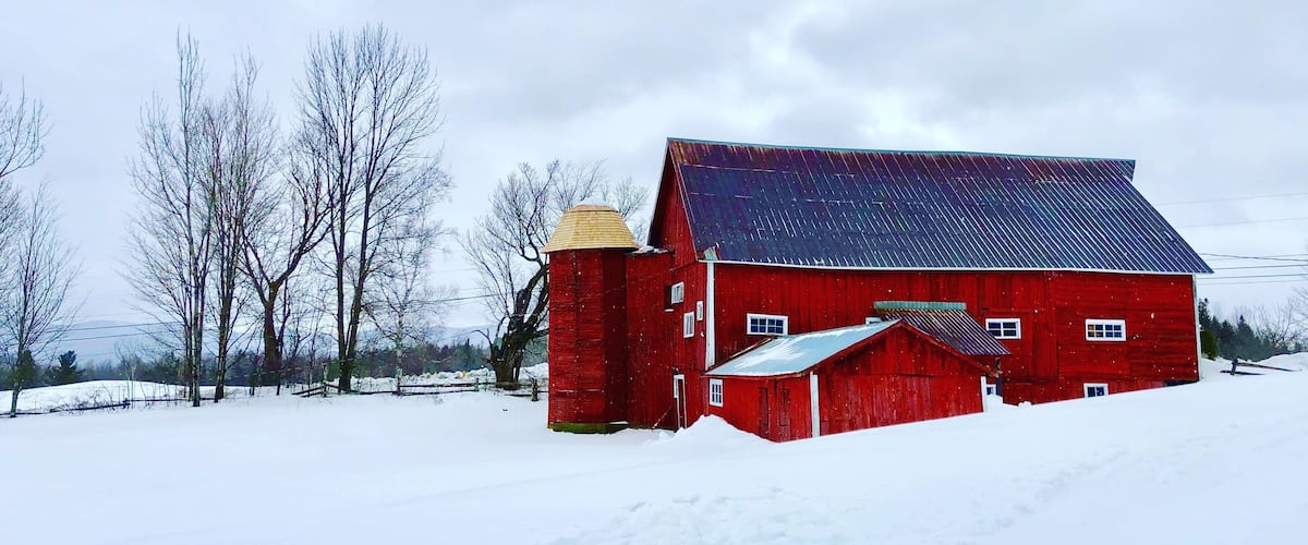 A red barn with a metal roof in a snowy field.