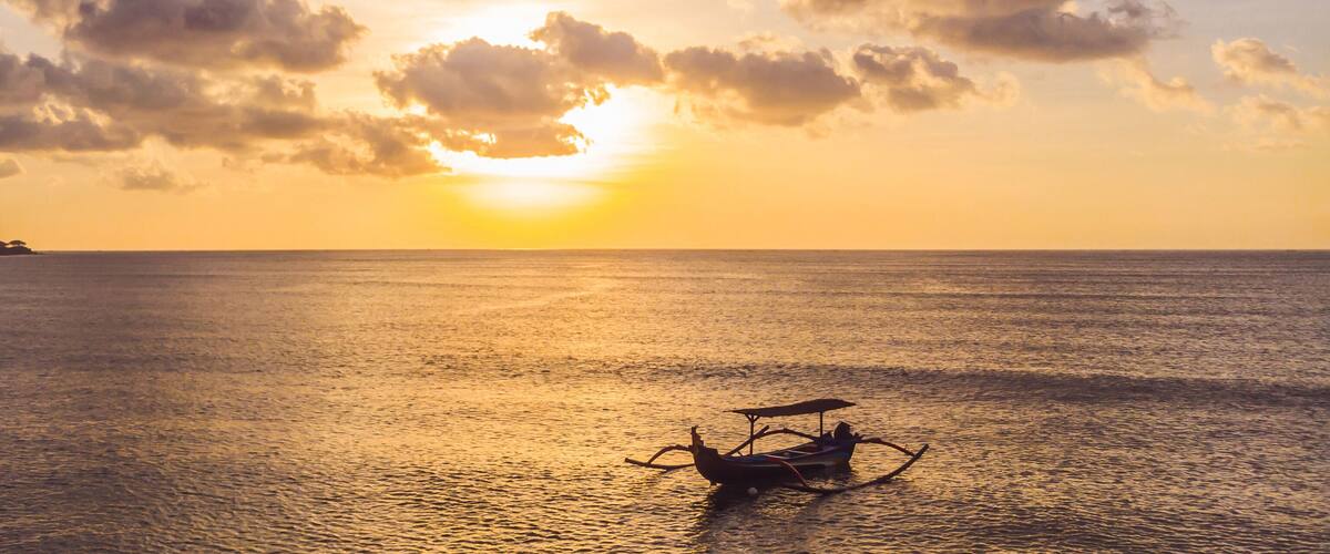 A sunset over a calm sea with a traditional boat in the foreground.