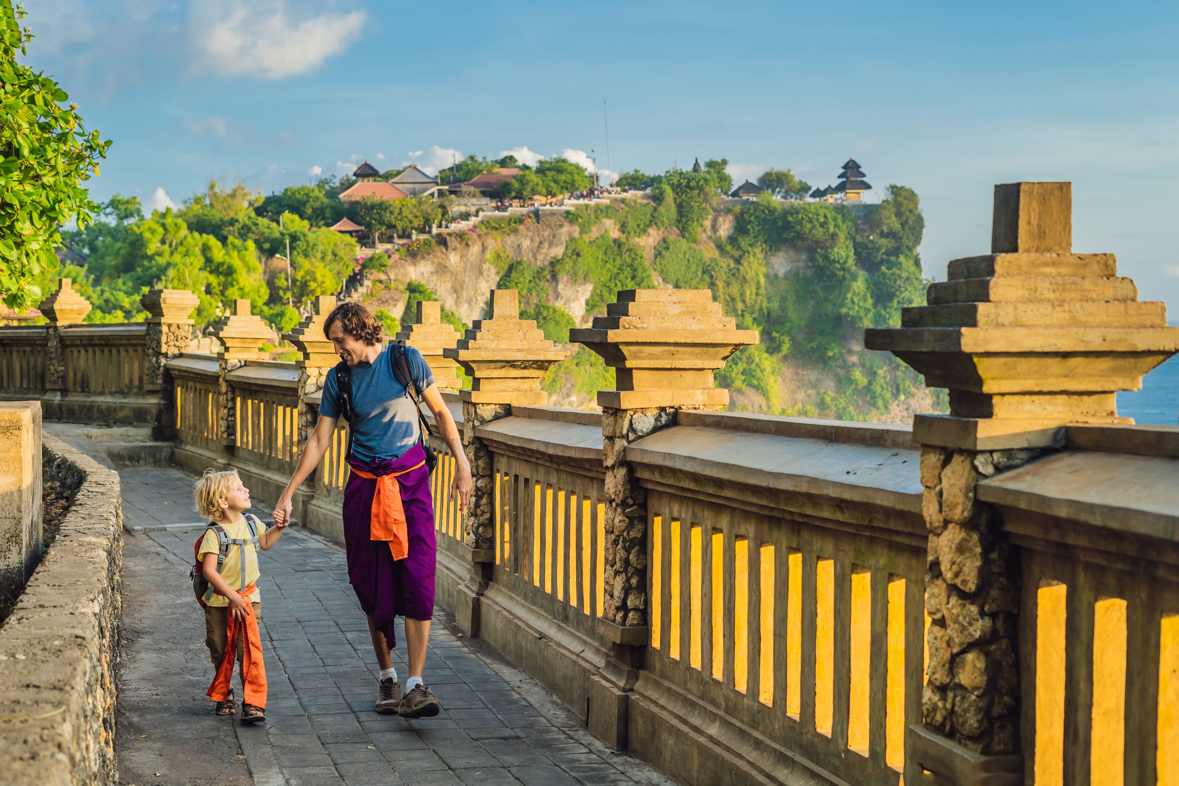 Dad and son travelers in Pura Luhur Uluwatu temple, Bali, Indonesia. Amazing landscape - cliff with blue sky and sea. Traveling with kids concept