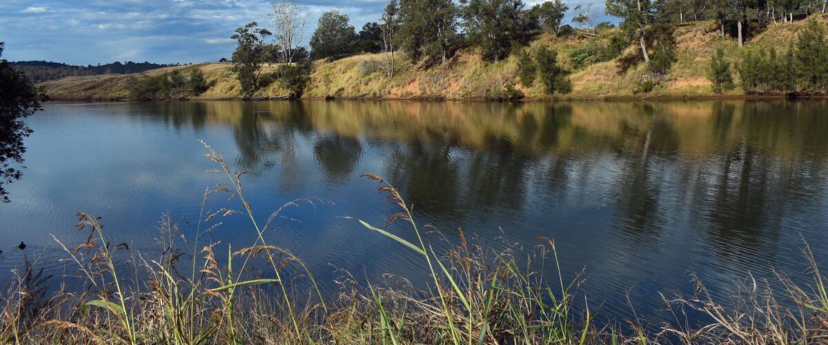 A calm lake with reflections of trees and sky, surrounded by grassy hills and sparse vegetation.