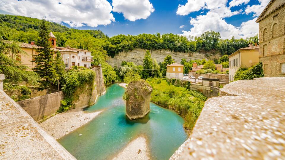 A river with a large rock in the middle, surrounded by houses and greenery.