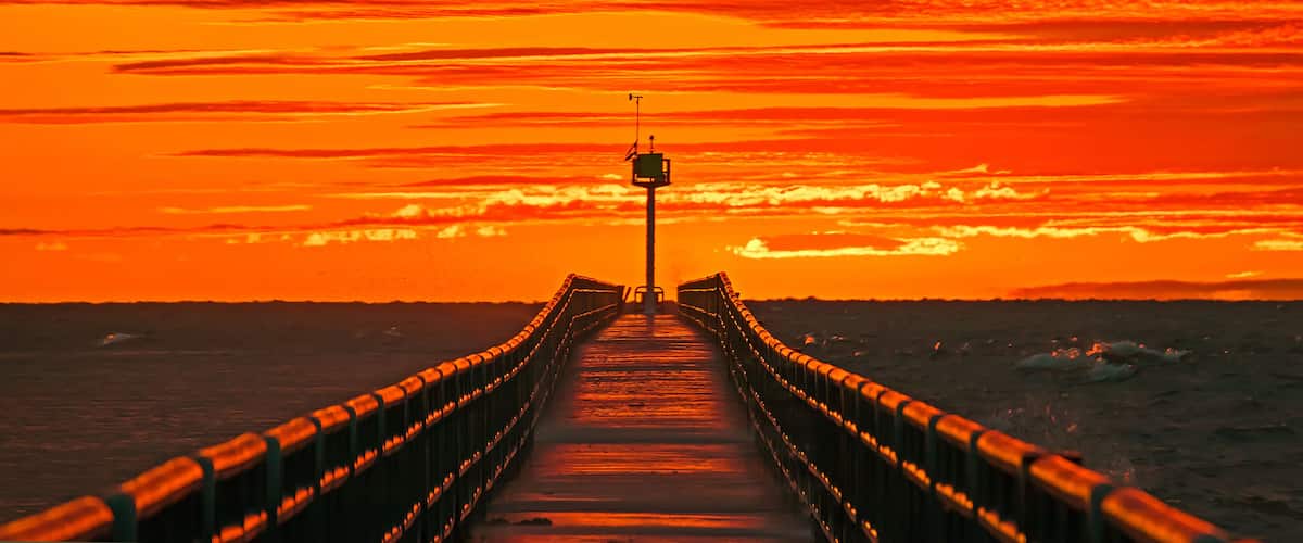 A pier extending into a body of water with a sunset in the background.