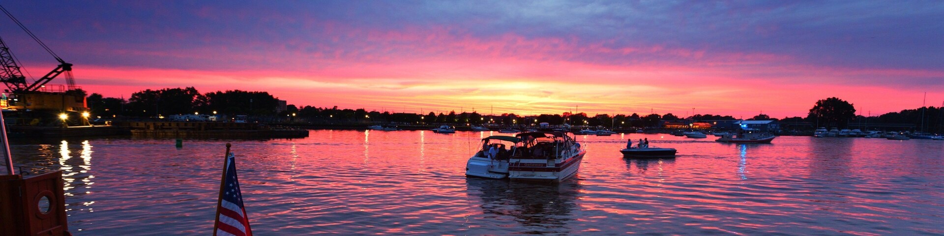 Atardecer sobre un puerto con barcos y una bandera.