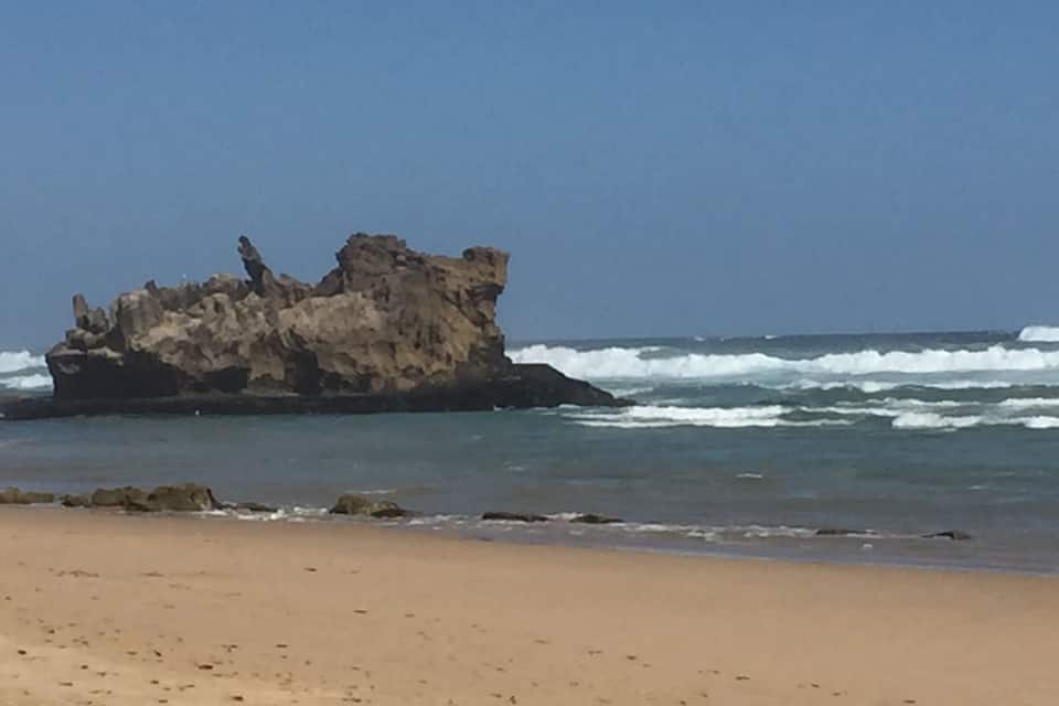 A rocky outcrop on a beach with waves crashing against it.