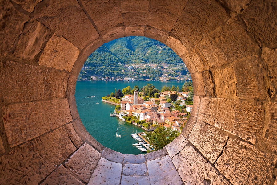 Un arco de piedra con vistas a un pueblo junto a un lago, con barcos y una iglesia.