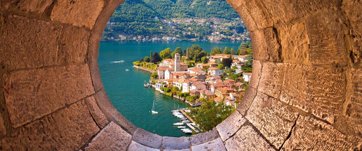 A stone archway overlooking a town by a lake with boats and a church.