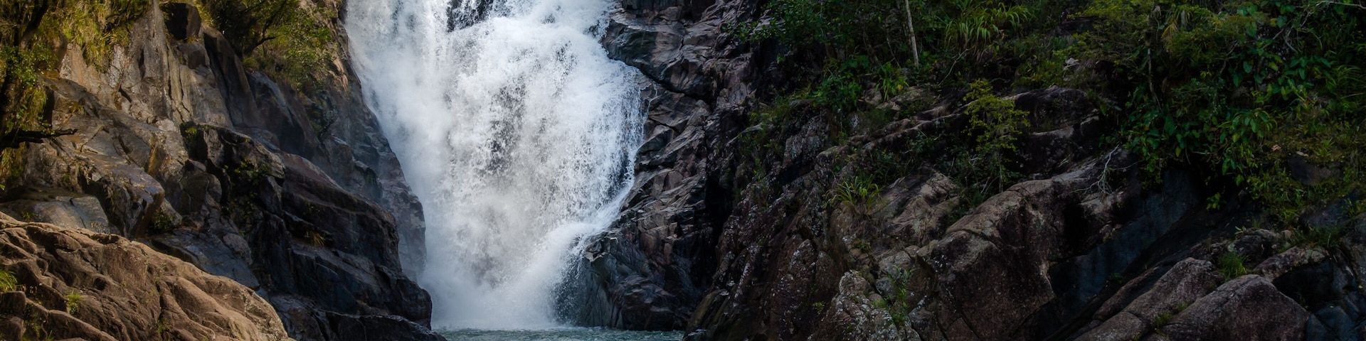 Uma cascata despencando sobre um penhasco rochoso em um rio, cercado por floresta densa.