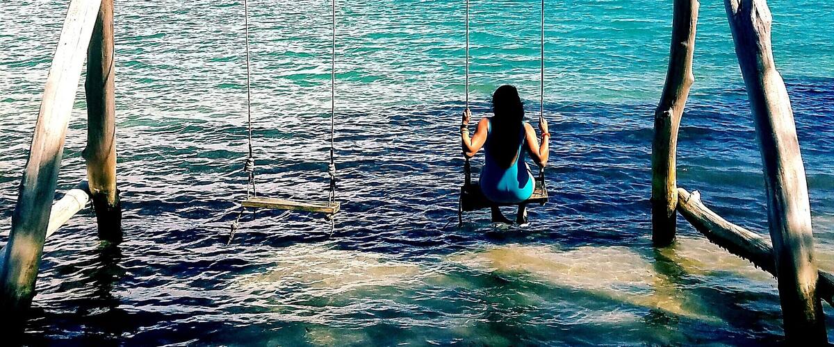 A wooden swing over water with a person sitting on it.