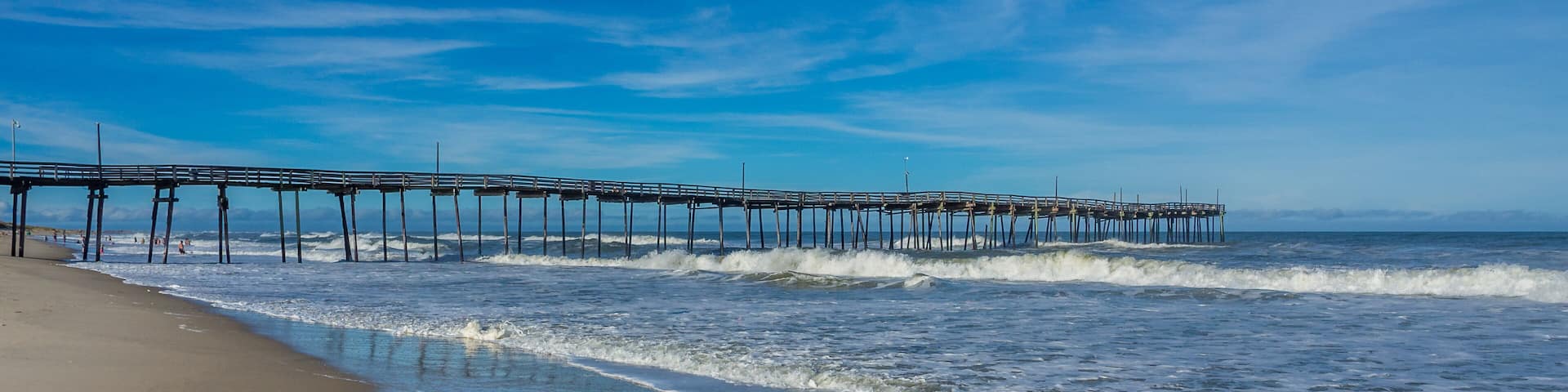 A beach with waves and a pier extending into the ocean.