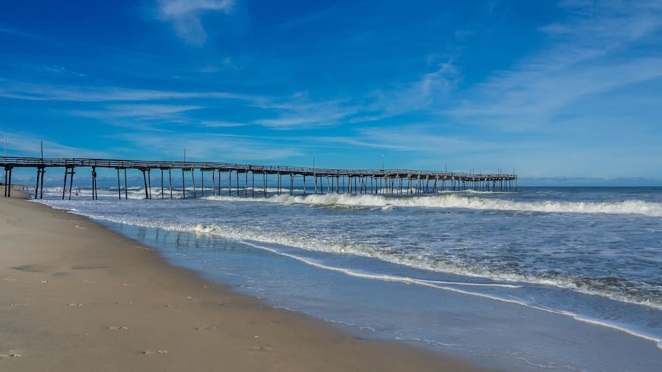A beach with waves and a pier extending into the ocean.