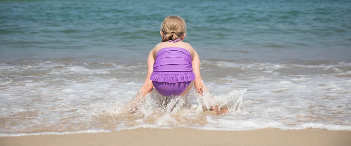 A beach with waves and a person in a purple swimsuit.
