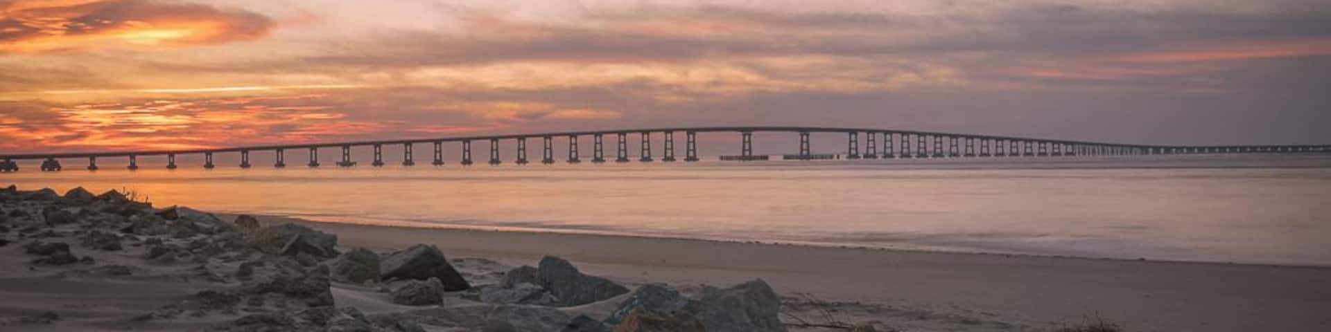 This image was captured at the Oregon Inlet on the NC Outerbanks in December of 2015. It features the iconic Bonner Bridge, one of the more famous bridges in North Carolina. This was an impromptu trip that I undertook hoping to catch a sight of Comet Catalina that was gracing our skies at the time. That trip turned out to be one of the best trips I have ever undertaken as I encountered perfect conditions for photography every single day over the 3 day period I was there.
This image is a blend of 2 images to bring out some detail in the foreground rocks. This composition appealed to me since the foreground rocks form a natural line to lead the viewer's eyes to the bridge and the clouds above. The clouds on this day were assuming various familiar shapes with the one captured here taking the shape of a bird in flight.
This particular stretch of the shoreline is very peaceful to walk along. Since it's an inlet, the waves are extremely calm unless it's windy. There are several sand dunes to the left of this image that ultimately would lead you to the proper coast and the ocean.
Update, 2020: This bridge is being dismantled and replaced with a newer bridge. Bonner Bridge has a lot of history tied to it and while it's sad to see it go, I feel fortunate to have captured part of this history personally.
Thank you for stopping by and for the support.
#sunset #nc #usa #bridge #obx #outerbanks #colorful #goldenhour #roadtrip #weekend #beach #beaches #bestof5 #nationalpark #bridges #lovemytown
#history #BeachBound