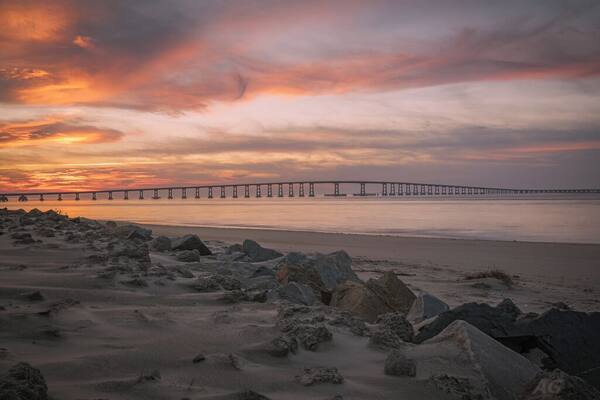 This image was captured at the Oregon Inlet on the NC Outerbanks in December of 2015. It features the iconic Bonner Bridge, one of the more famous bridges in North Carolina. This was an impromptu trip that I undertook hoping to catch a sight of Comet Catalina that was gracing our skies at the time. That trip turned out to be one of the best trips I have ever undertaken as I encountered perfect conditions for photography every single day over the 3 day period I was there.
This image is a blend of 2 images to bring out some detail in the foreground rocks. This composition appealed to me since the foreground rocks form a natural line to lead the viewer's eyes to the bridge and the clouds above. The clouds on this day were assuming various familiar shapes with the one captured here taking the shape of a bird in flight.
This particular stretch of the shoreline is very peaceful to walk along. Since it's an inlet, the waves are extremely calm unless it's windy. There are several sand dunes to the left of this image that ultimately would lead you to the proper coast and the ocean.
Update, 2020: This bridge is being dismantled and replaced with a newer bridge. Bonner Bridge has a lot of history tied to it and while it's sad to see it go, I feel fortunate to have captured part of this history personally.
Thank you for stopping by and for the support.
#sunset #nc #usa #bridge #obx #outerbanks #colorful #goldenhour #roadtrip #weekend #beach #beaches #bestof5 #nationalpark #bridges #lovemytown
#history #BeachBound