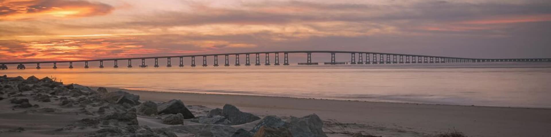 This image was captured at the Oregon Inlet on the NC Outerbanks in December of 2015. It features the iconic Bonner Bridge, one of the more famous bridges in North Carolina. This was an impromptu trip that I undertook hoping to catch a sight of Comet Catalina that was gracing our skies at the time. That trip turned out to be one of the best trips I have ever undertaken as I encountered perfect conditions for photography every single day over the 3 day period I was there.
This image is a blend of 2 images to bring out some detail in the foreground rocks. This composition appealed to me since the foreground rocks form a natural line to lead the viewer's eyes to the bridge and the clouds above. The clouds on this day were assuming various familiar shapes with the one captured here taking the shape of a bird in flight.
This particular stretch of the shoreline is very peaceful to walk along. Since it's an inlet, the waves are extremely calm unless it's windy. There are several sand dunes to the left of this image that ultimately would lead you to the proper coast and the ocean.
Update, 2020: This bridge is being dismantled and replaced with a newer bridge. Bonner Bridge has a lot of history tied to it and while it's sad to see it go, I feel fortunate to have captured part of this history personally.
Thank you for stopping by and for the support.
#sunset #nc #usa #bridge #obx #outerbanks #colorful #goldenhour #roadtrip #weekend #beach #beaches #bestof5 #nationalpark #bridges #lovemytown
#history #BeachBound