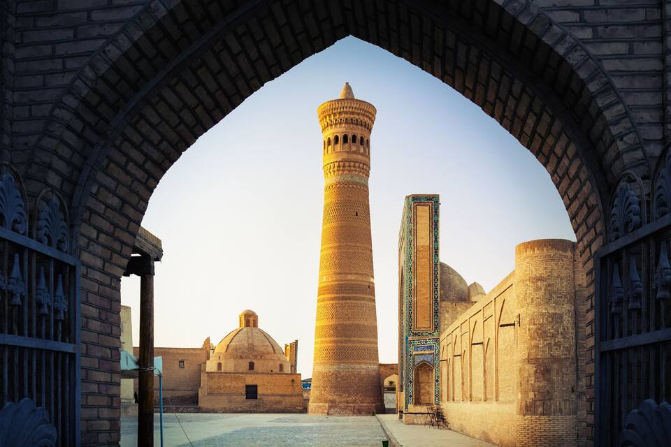 An arched gateway leading to a mosque with a tall minaret and a dome.