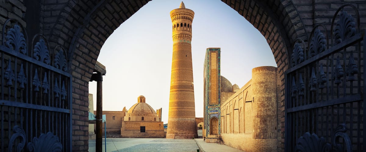 An arched gateway leading to a mosque with a tall minaret and a dome.