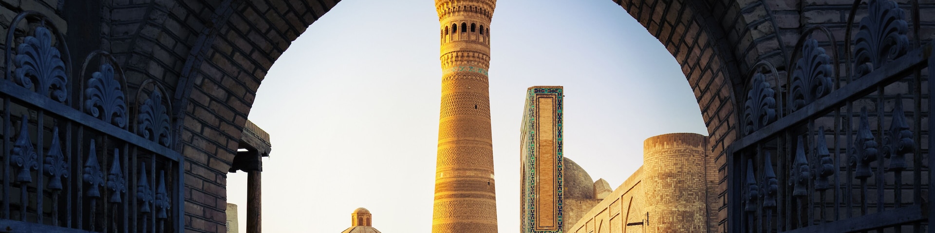 An arched gateway leading to a mosque with a tall minaret and a dome.