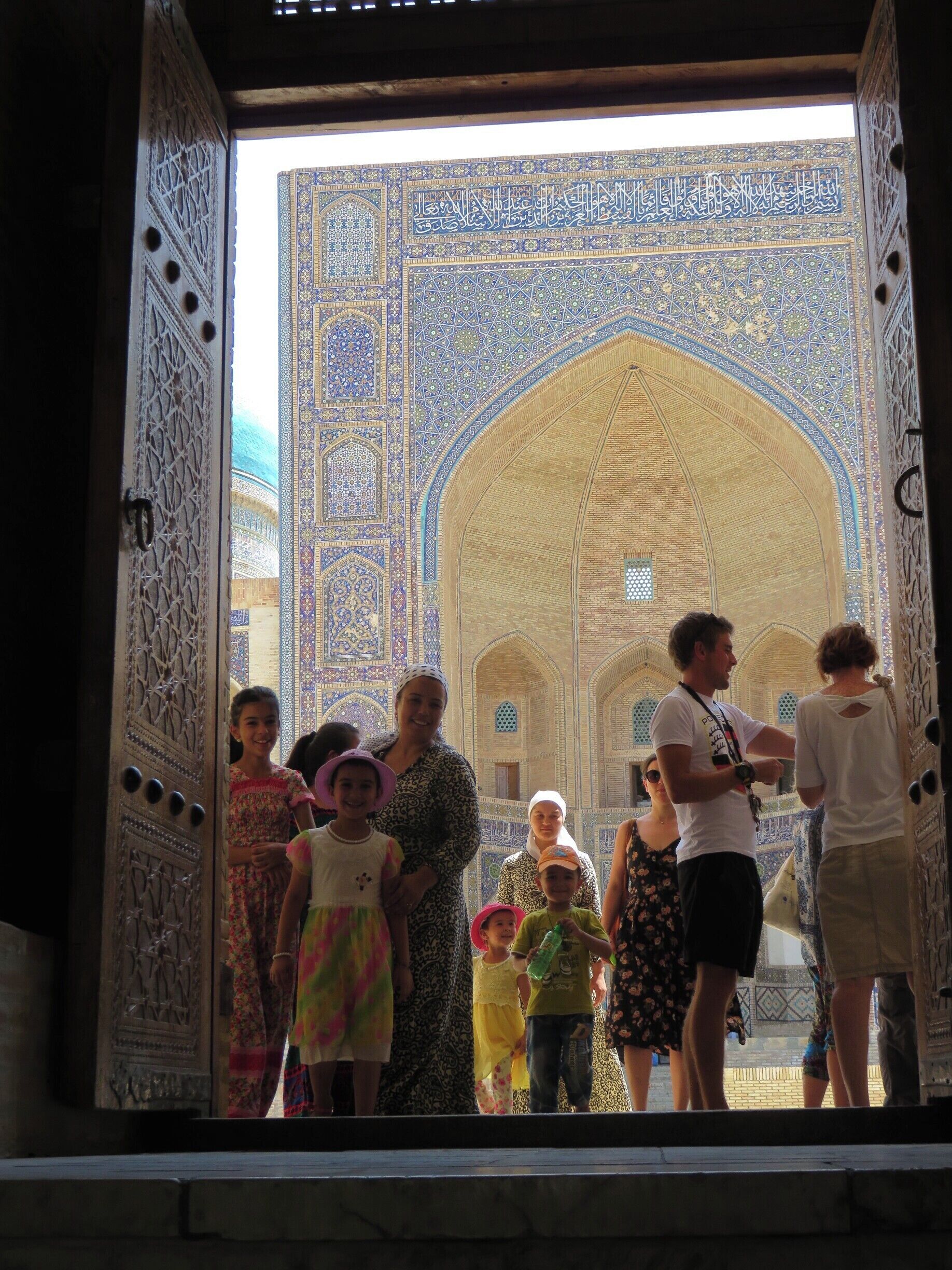 The view from inside the Kalyon Mosque outwards into the opposite portal is stunning as it catches the morning's sun rays. Here you see a gaggle of Uzbeks and fellow travellers at the entrance. #colorful