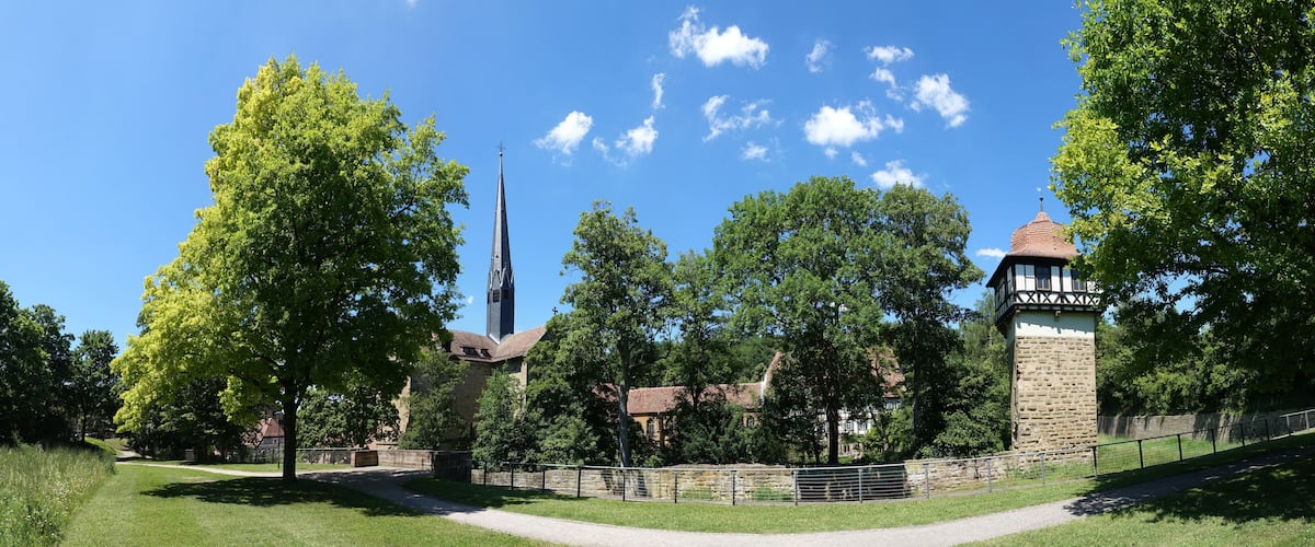 A church with a tall steeple, surrounded by trees and a stone tower.