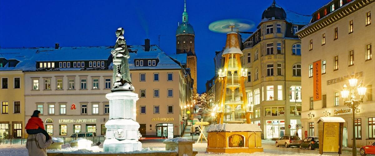 A snow-covered square with a fountain, historic buildings, and a clock tower.