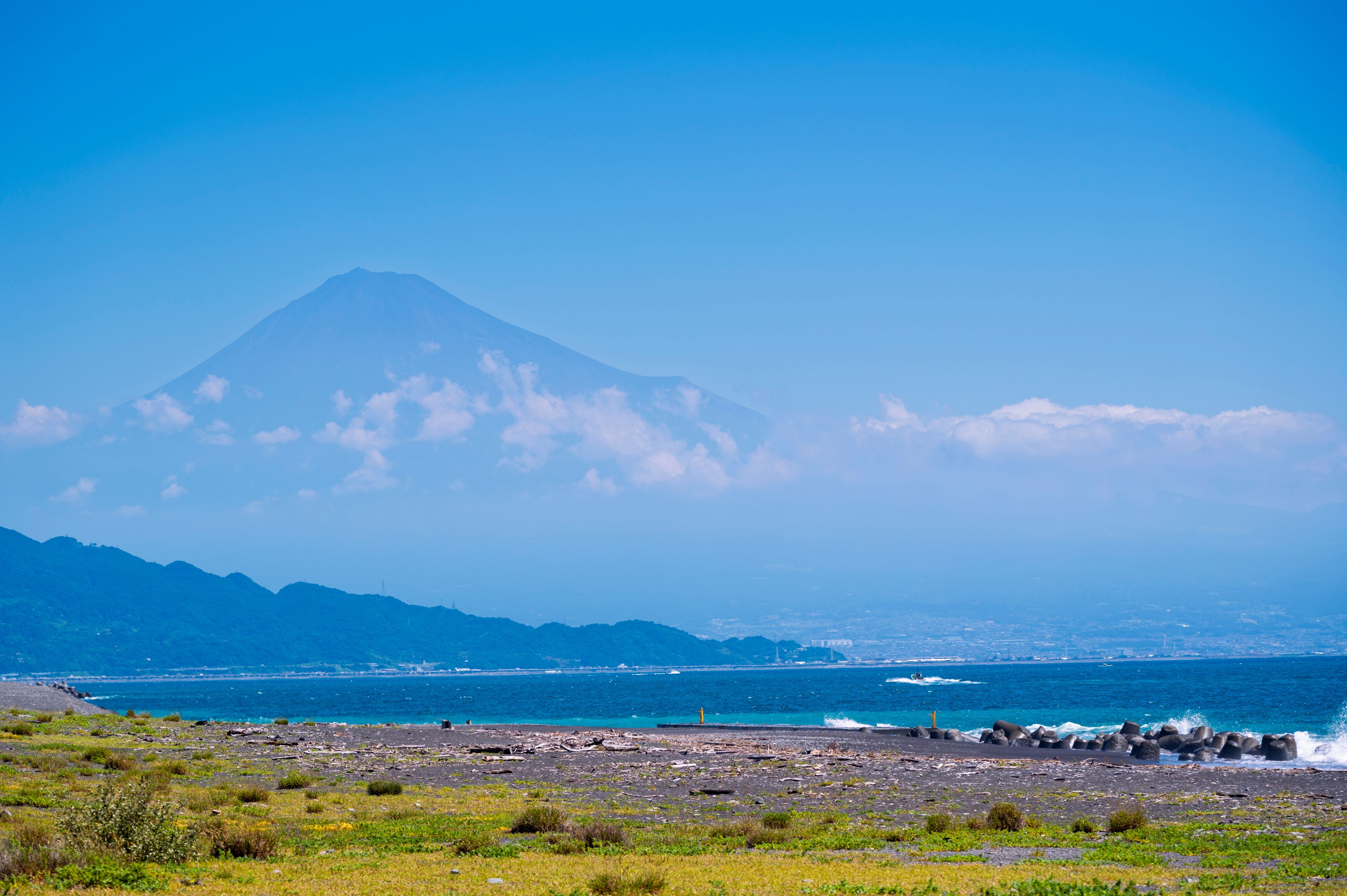 A coastal landscape with a prominent mountain in the background, a rocky shoreline, and a clear blue sky.