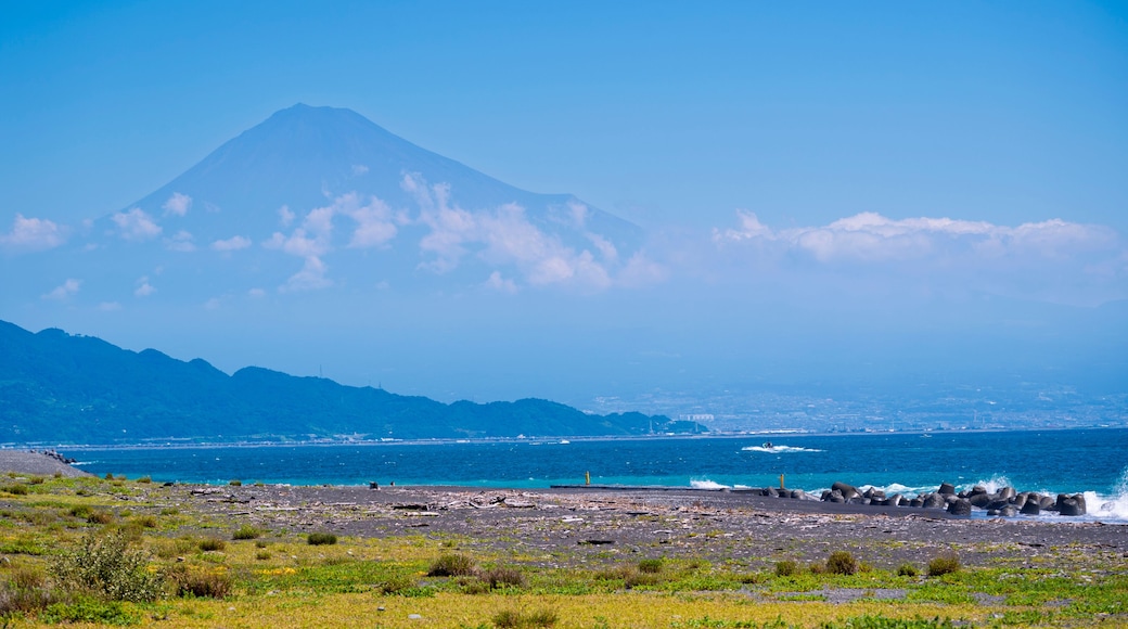 A coastal landscape with a prominent mountain in the background, a rocky shoreline, and a clear blue sky.