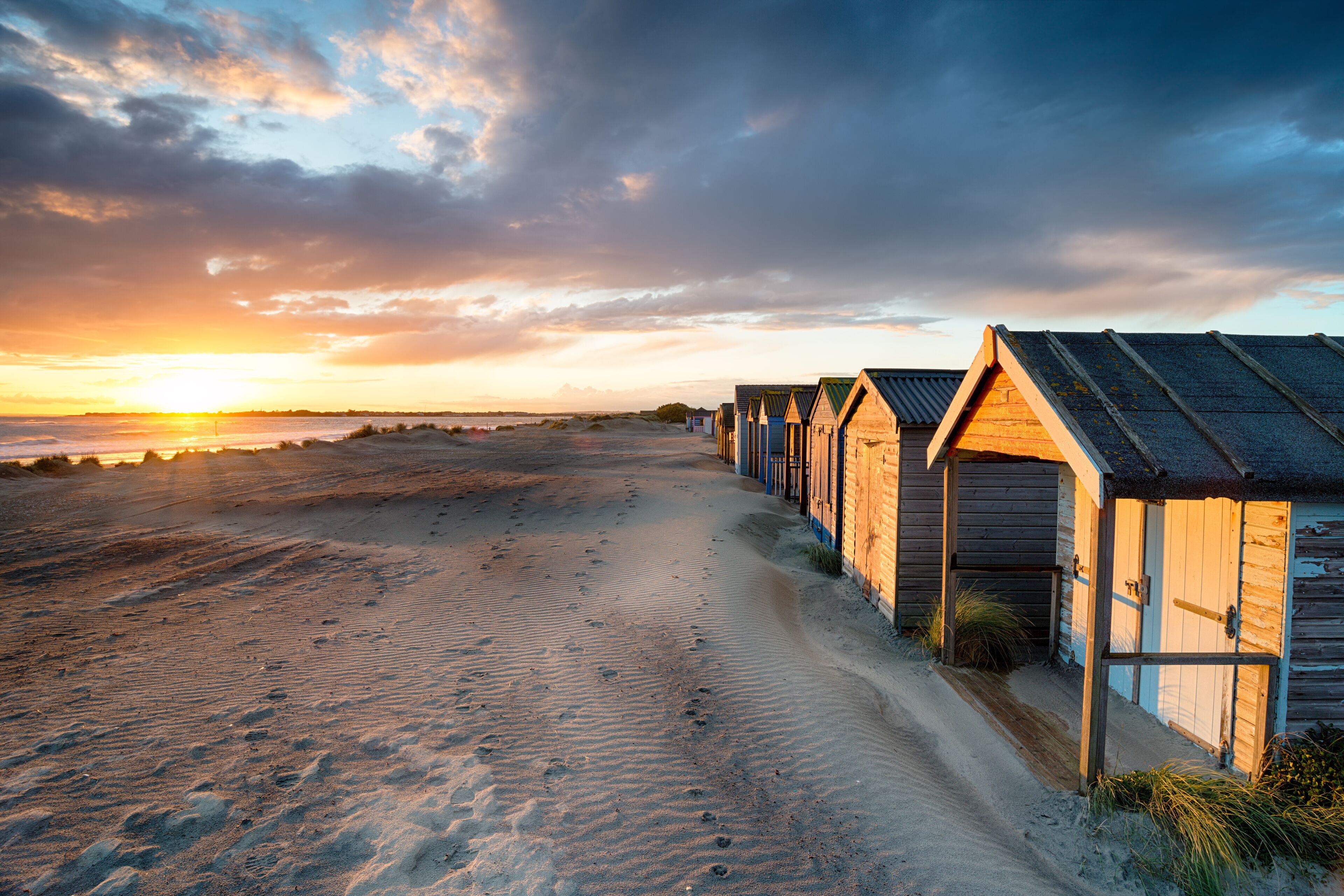 A beach with wooden beach huts and a sunset in the background.