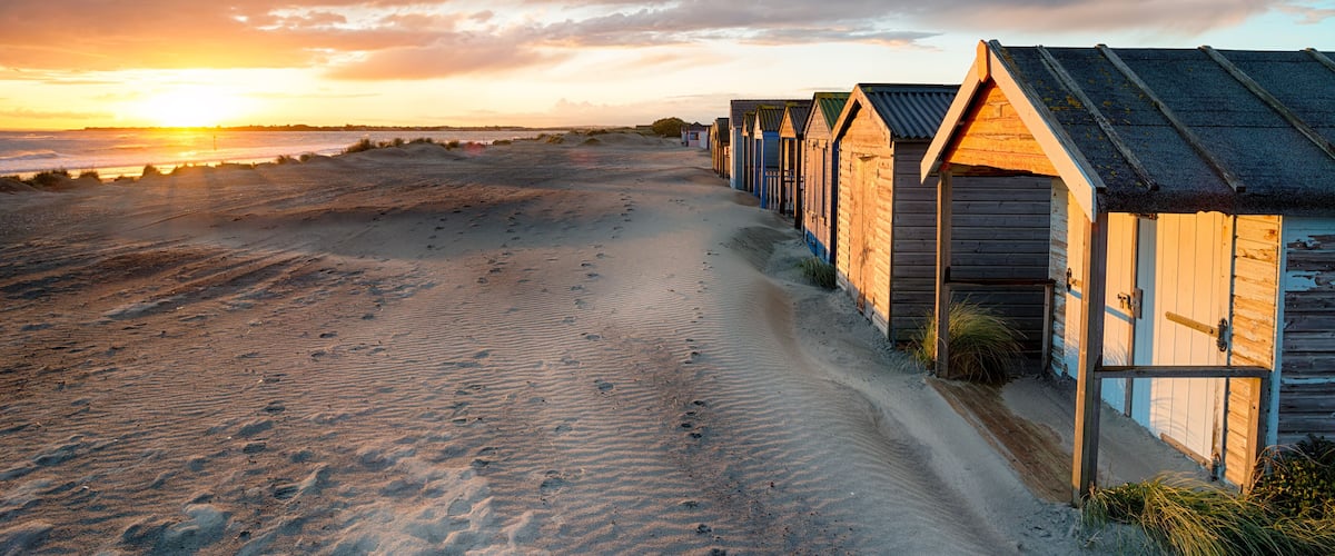 A beach with wooden beach huts and a sunset in the background.