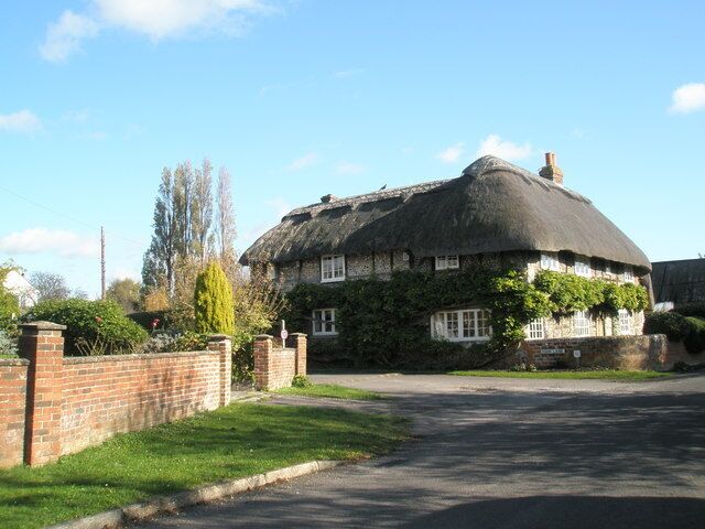 A thatched-roof house with ivy, a brick wall, and a clear sky.