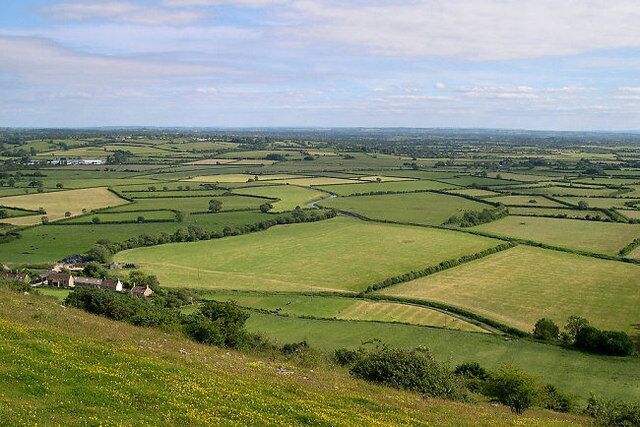 Rolling green fields, a small house, and distant hills.