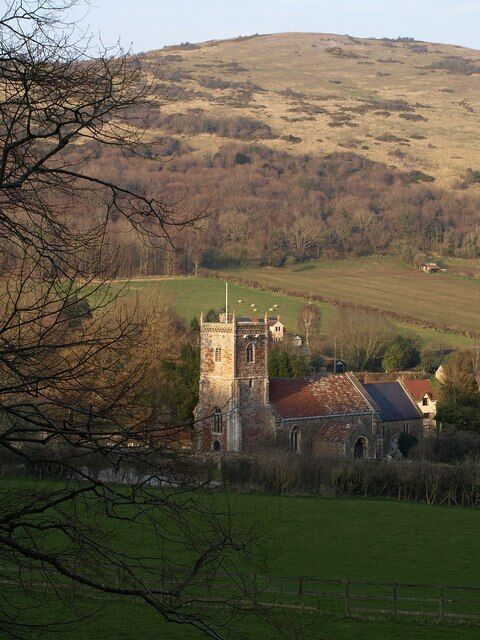 A historic church with a bell tower, surrounded by rolling hills and fields.