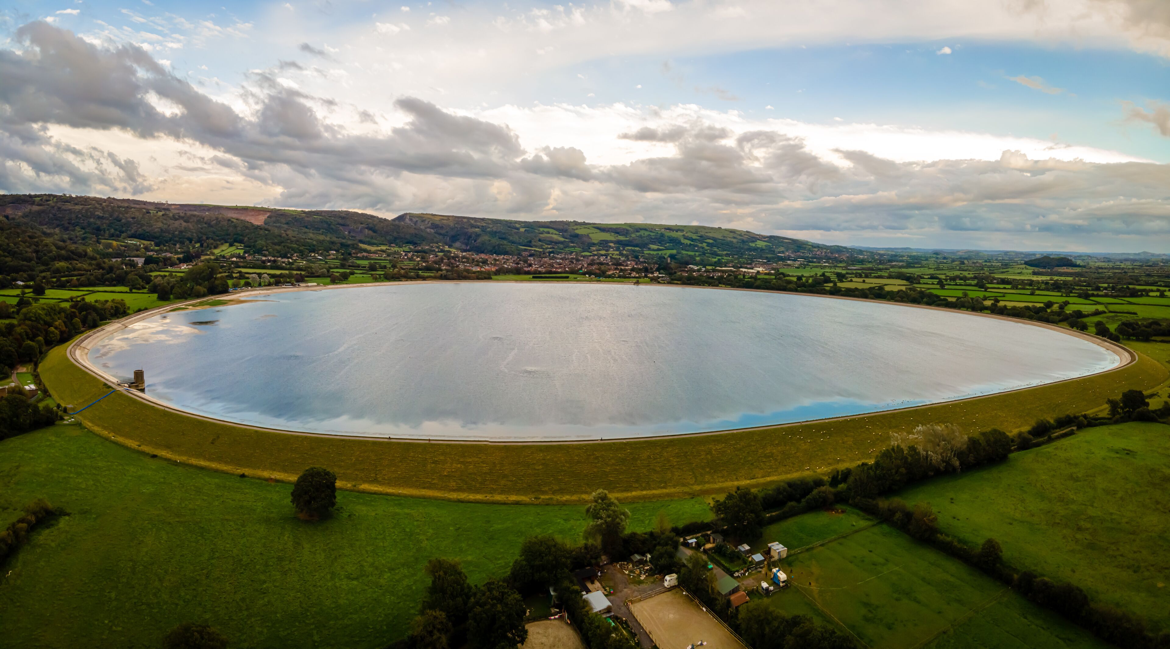 An aerial view of a large, circular water body surrounded by green fields and a small village.