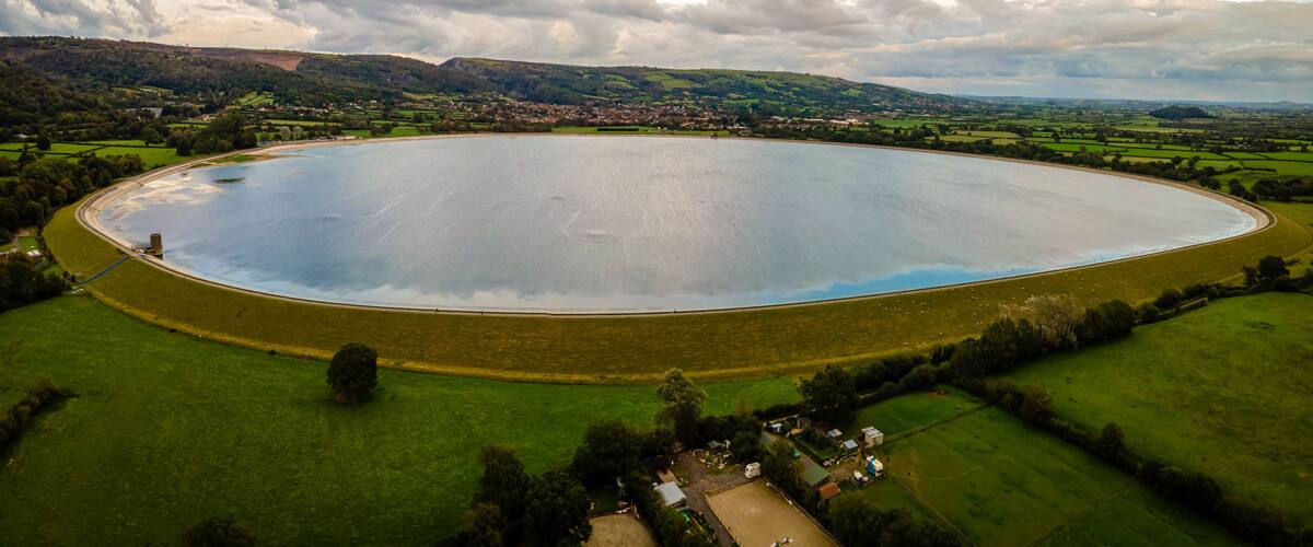 An aerial view of a large, circular water body surrounded by green fields and a small village.