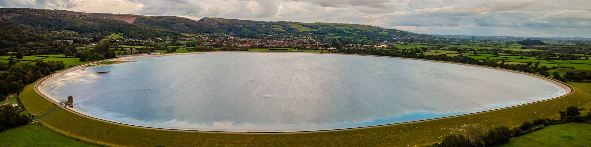 An aerial view of a large, circular water body surrounded by green fields and a small village.