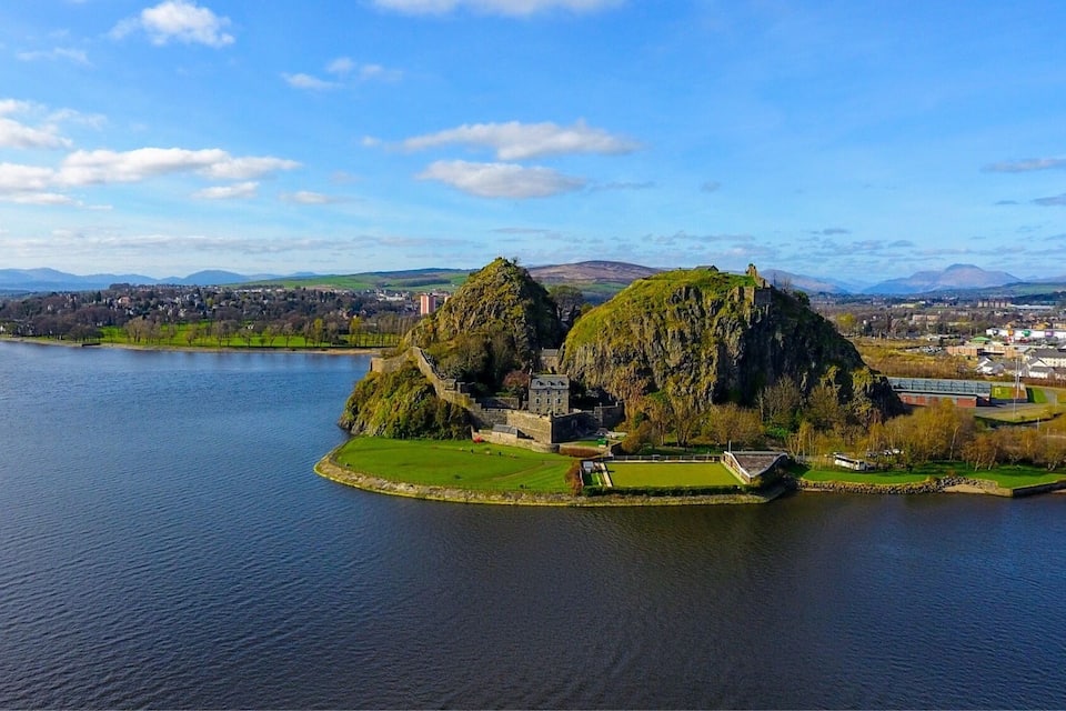 Un paisaje costero con una isla rocosa destacada y un pueblo al fondo.