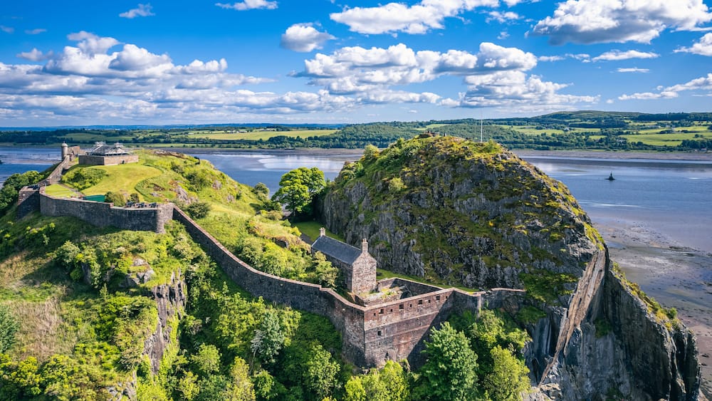 A historic fortification overlooking a river, surrounded by lush greenery and hills.