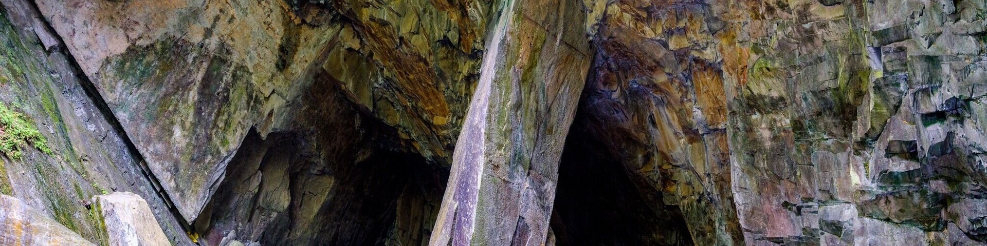 Entrada de caverna cercada por pedras grandes e um pequeno corpo de água.
