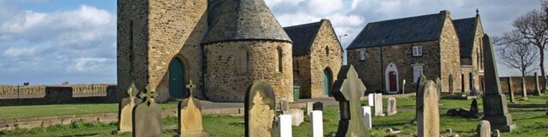 Una iglesia histórica con una torre destacada y varios mausoleos en un cementerio.