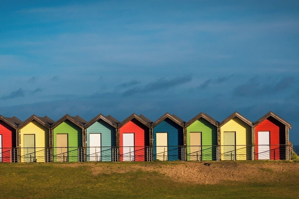 Une rangée de cabanes de plage colorées, avec une éolienne en arrière-plan.