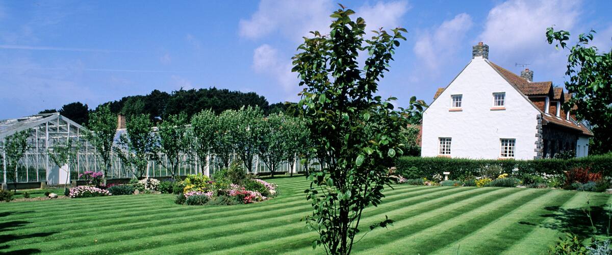 A well-manicured lawn, a white house, and a greenhouse in a garden.