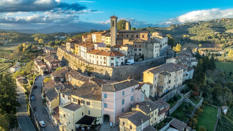 A historic town with a prominent tower, terraced buildings, and a surrounding hilly landscape.