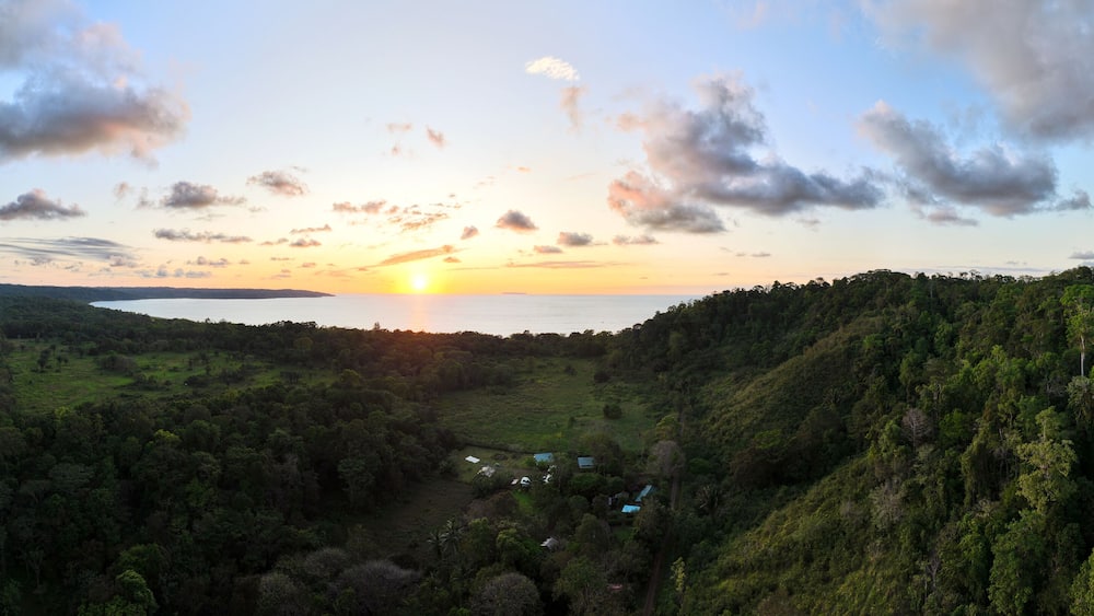 A sunset over a valley with a lake, surrounded by dense forest and hills.
