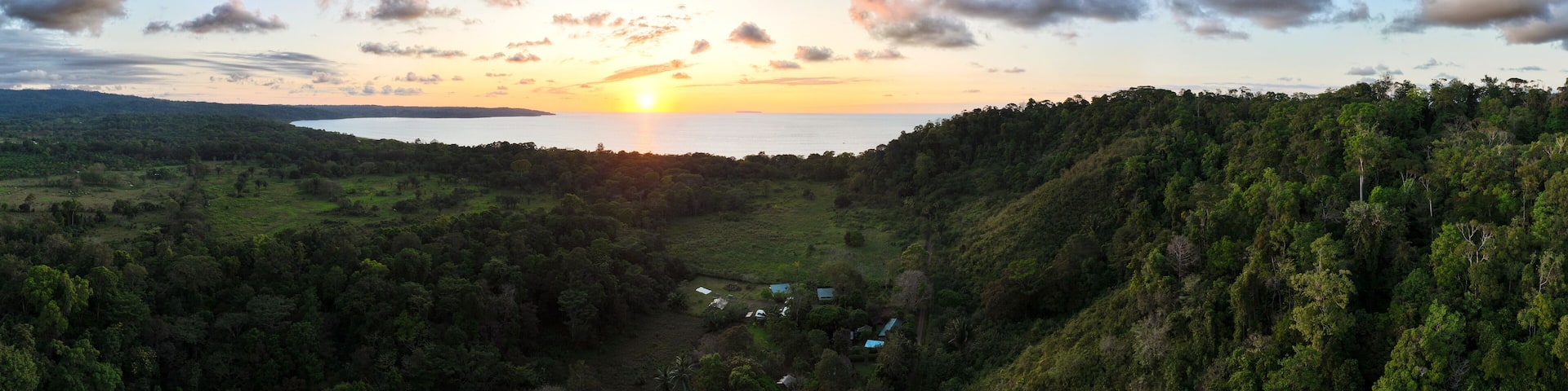 Wide aerial panorama of sunset over rural Costa Rica forest looking out towards the ocean and the setting sun. Drone photo taken near Drake Bay.