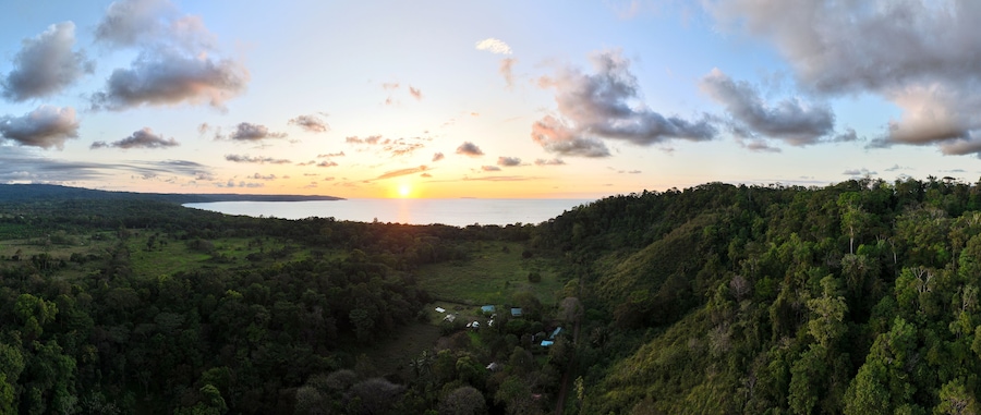 Un atardecer sobre un valle con un lago, rodeado de un bosque denso y colinas.