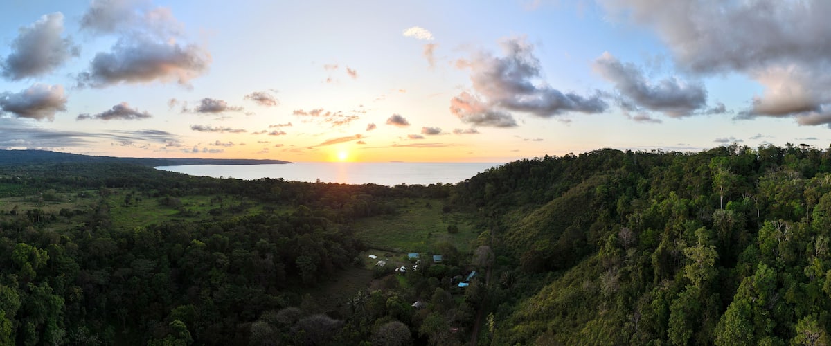 A sunset over a valley with a lake, surrounded by dense forest and hills.