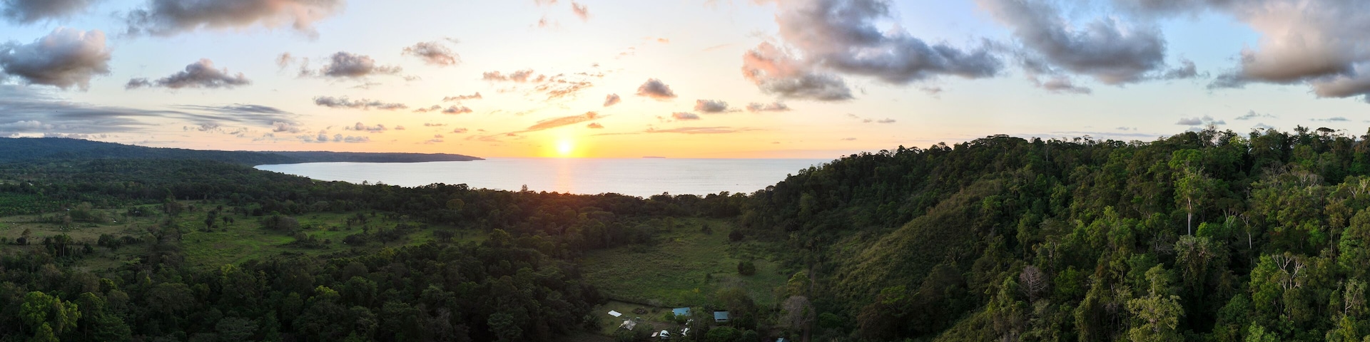 A sunset over a valley with a lake, surrounded by dense forest and hills.
