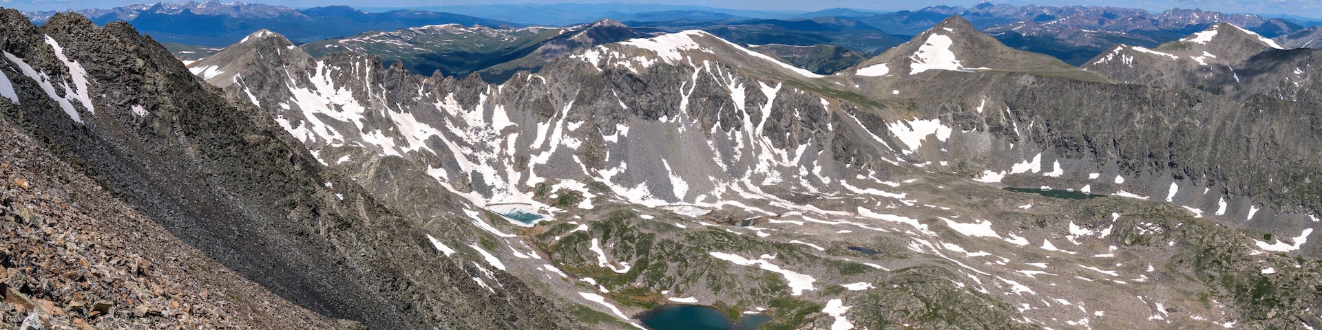 A mountainous landscape with rocky terrain, patches of snow, and a small lake.