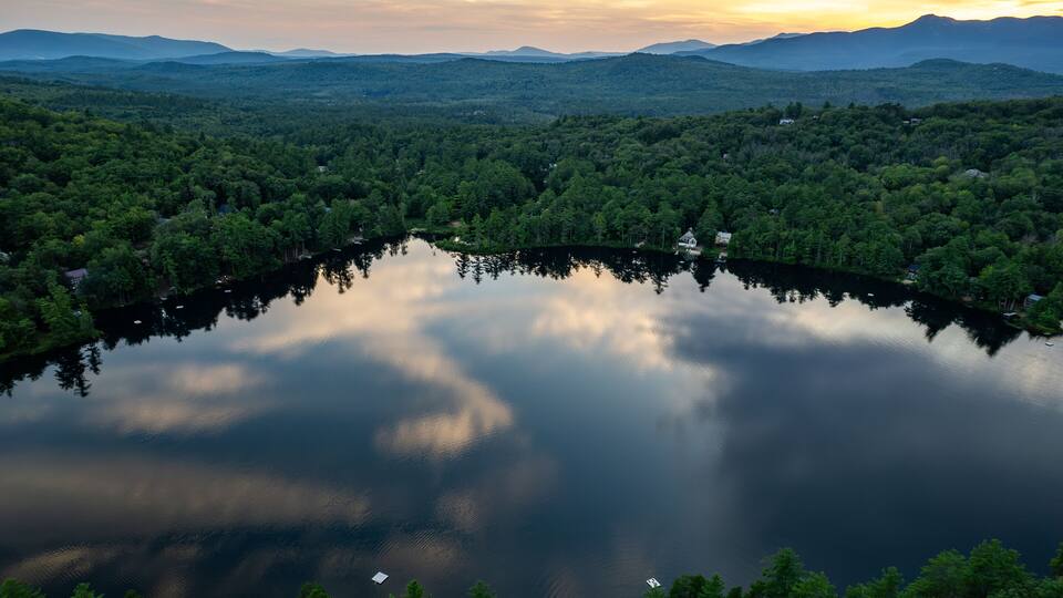 A lake surrounded by dense forest and mountains in the background.