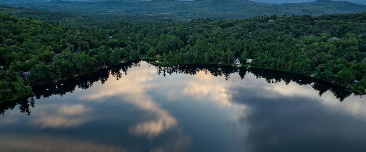 A lake surrounded by dense forest and mountains in the background.